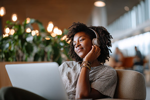 Young woman enjoying music while working on laptop, a Business Photo by AlyaAnd