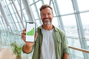 Young businessman celebrating success with smartphone display in modern office, a Business Photo by AlyaAnd