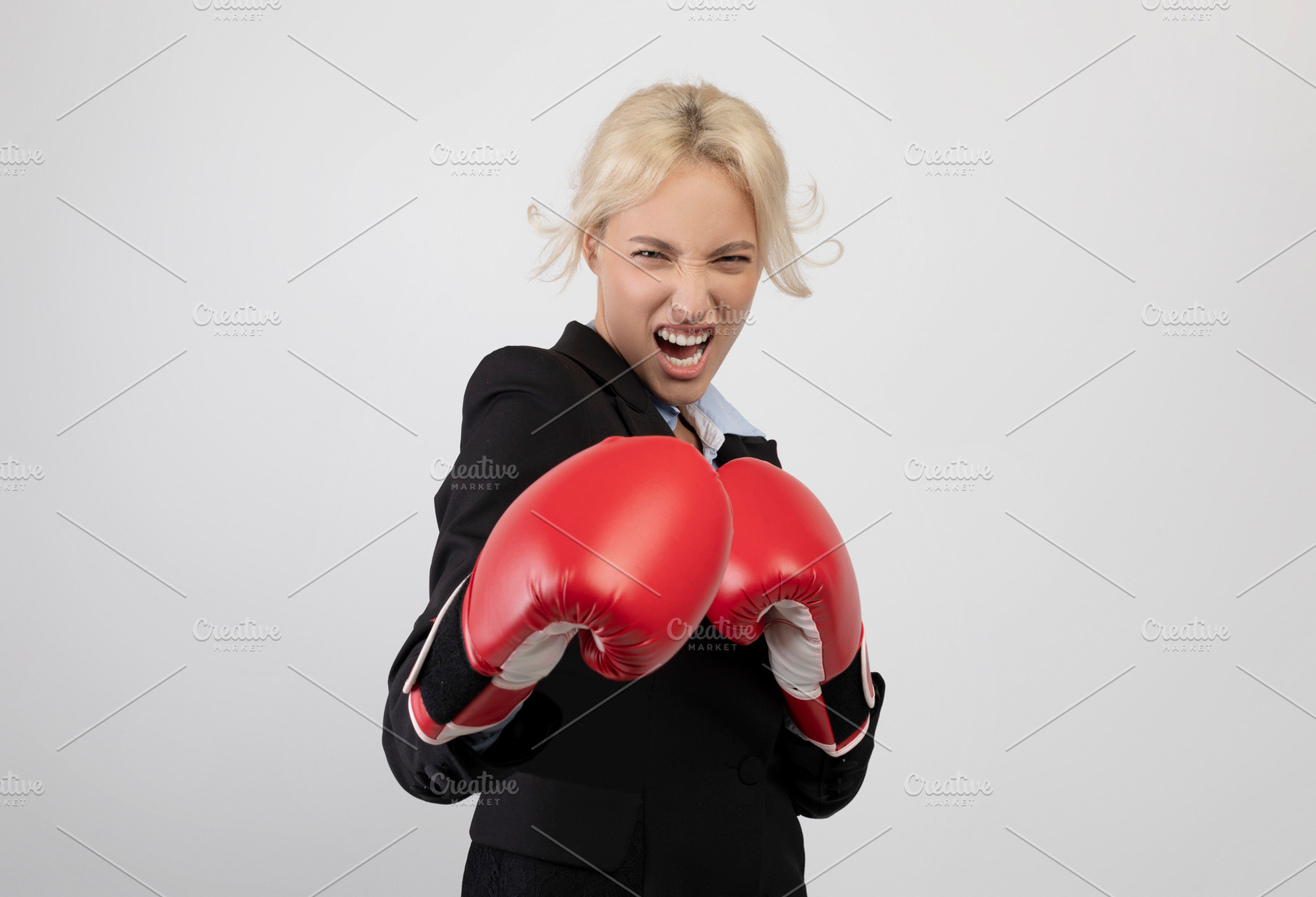 Angry young businesswoman in boxing gloves ready for fight over light grey back, a Photo by Prostock-Studio