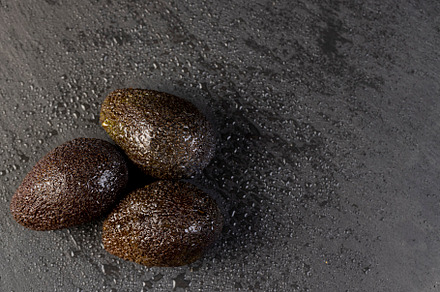 wet avocado fruits of small size on a black slate, ripe avocado fruit in drops