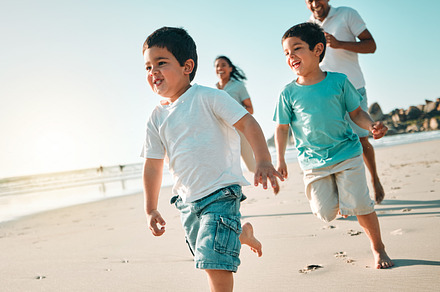 Happy, family and boys on a beach, running and summer vacation for bonding, loving and quality time. Run, mother and father with male children, kids and fitness on seaside holiday, happiness and joy, a Photo by Peopleimages.com