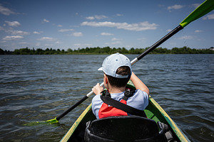 Child kayaking in calm lake water under a sunny blue sky, a Photo by AS photostudio