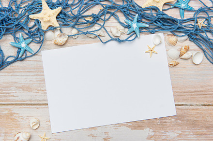 Fishing net, seashells and starfishes framing blank paper on woo