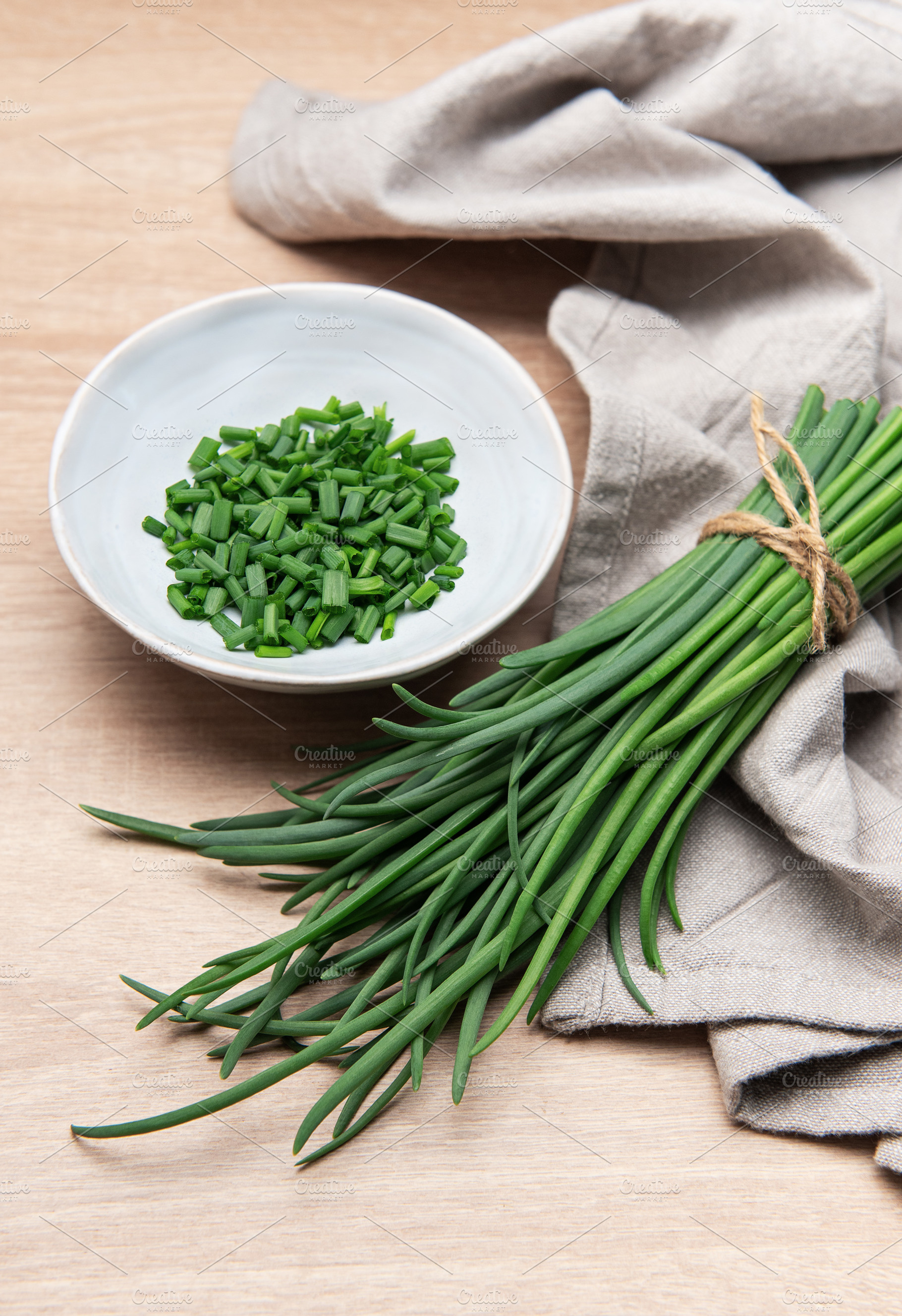Freshly cut chives in a bowl resting on wooden table, a Food & Drink Photo by Olena Rudo
