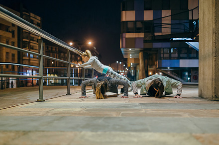 Female sport team doing push ups during training on the city at