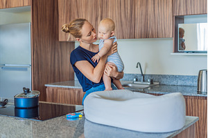 Mother holding baby while cooking, a Food & Drink Photo by Elizaveta Galitskaya