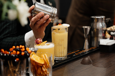 A bartender adds spices to a yellow cocktail.