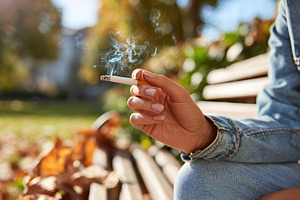 Smoker relaxing on a park bench surrounded by autumn leaves in a sunny afternoo, a Photo by AlyaAnd