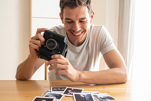 Man holding analog camara while smiling at looking print photo o, a Person Photo by DanFLCreativo