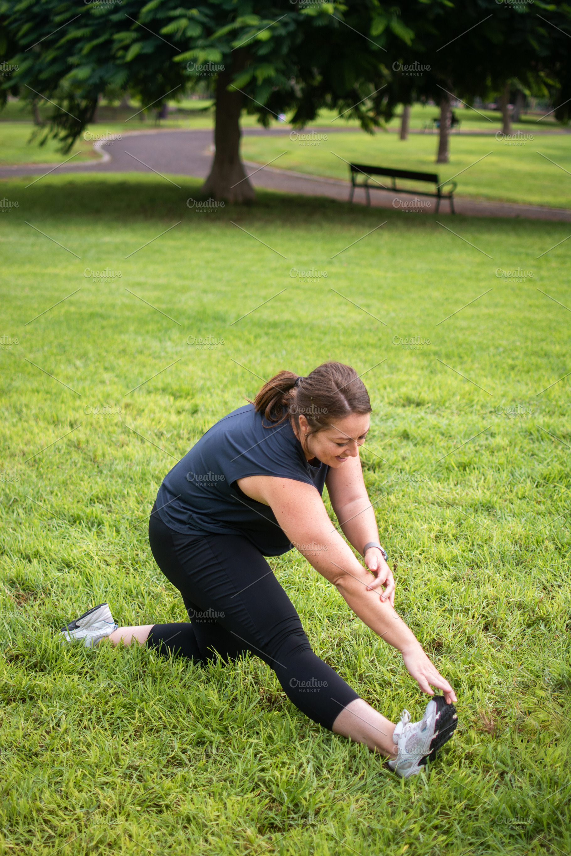 Woman stretching her leg on grass during outdoor fitness workout, a Photo by etorres69