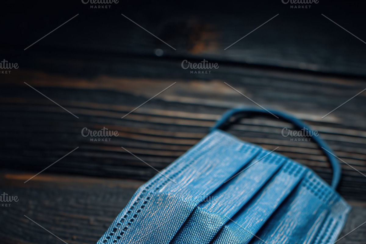 A blue surgical mask mockup lying on a dark wooden surface, a Mask Mockup by Textures & Backgrounds