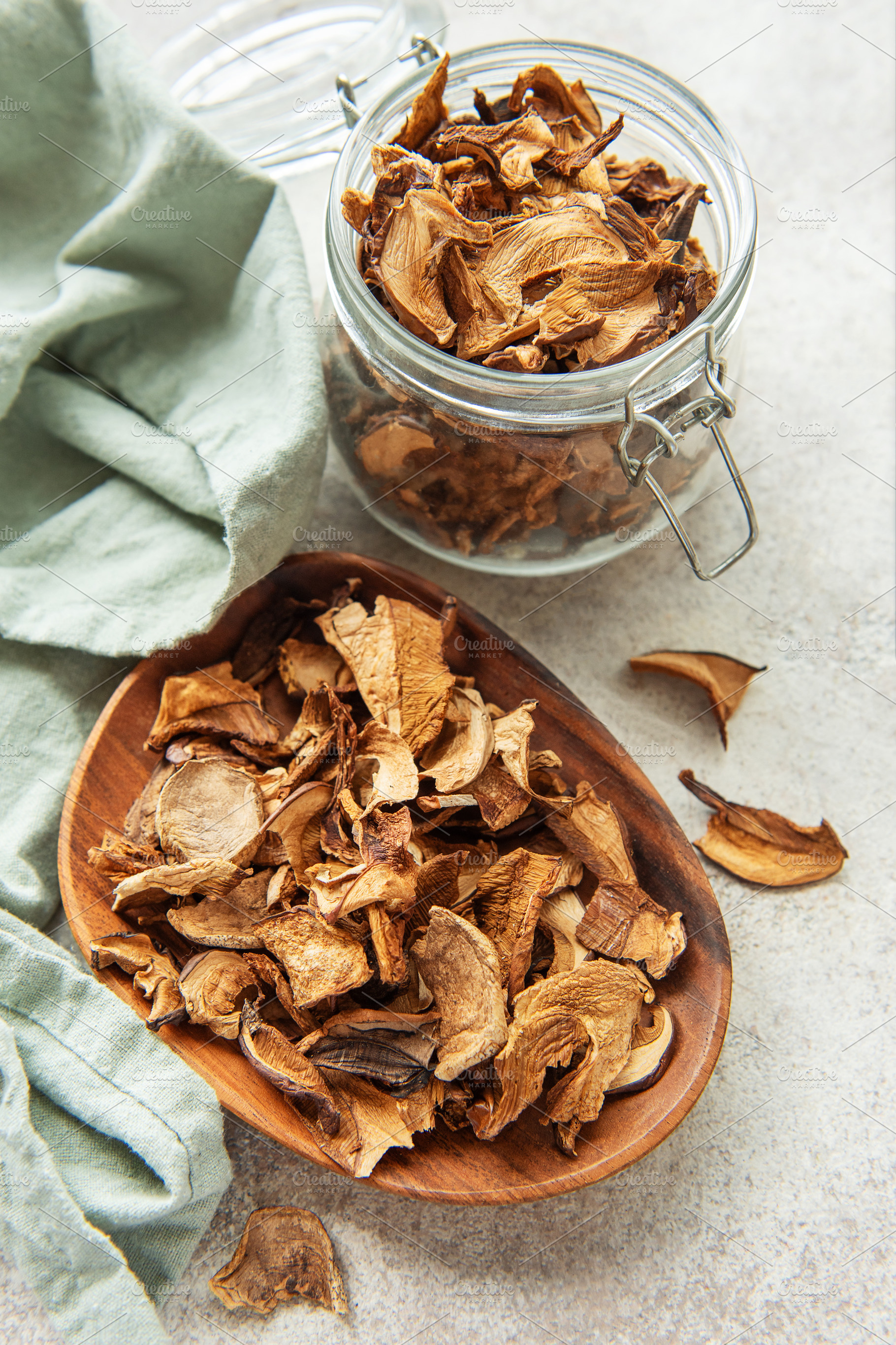 Dried mushrooms on wooden plate with fresh mushrooms and jar, a Food & Drink Photo by Olena Rudo