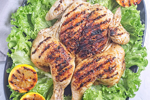 Spatchcocked grilled chicken with lemon garlic marinade on lettuce with lemon,, a Food & Drink Photo by iuliia_n