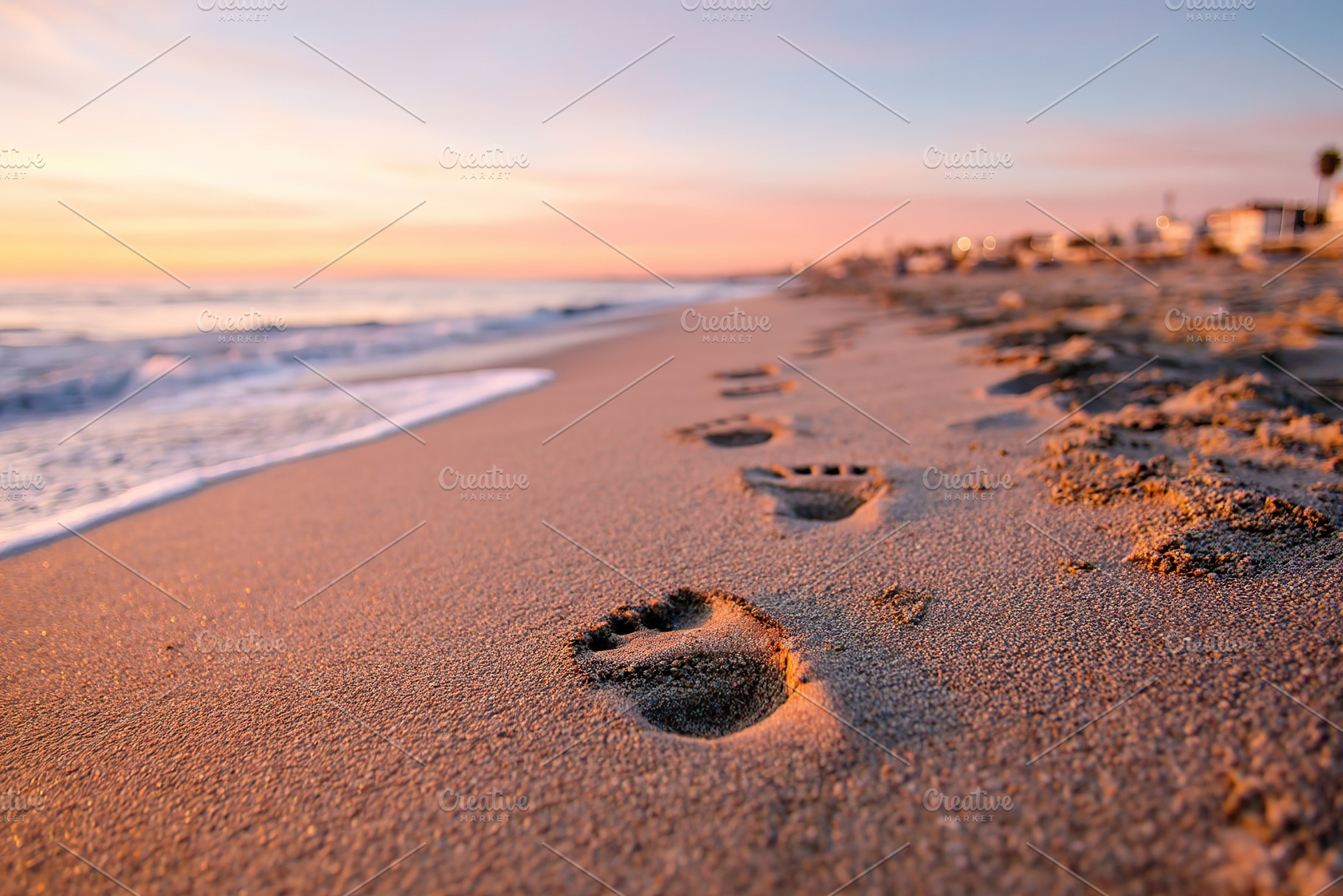 Footprints in light sand lead along a tranquil beach at sunset, a Photo by AlyaAnd