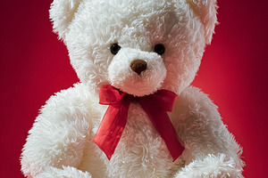 White teddy bear with red ribbon sitting on a vibrant red backgr, a Photo by Studio ANNA