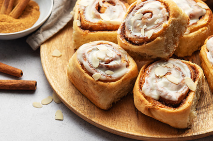 Freshly baked cinnamon rolls with icing and almond flakes on woo, a Food & Drink Photo by Olena Rudo
