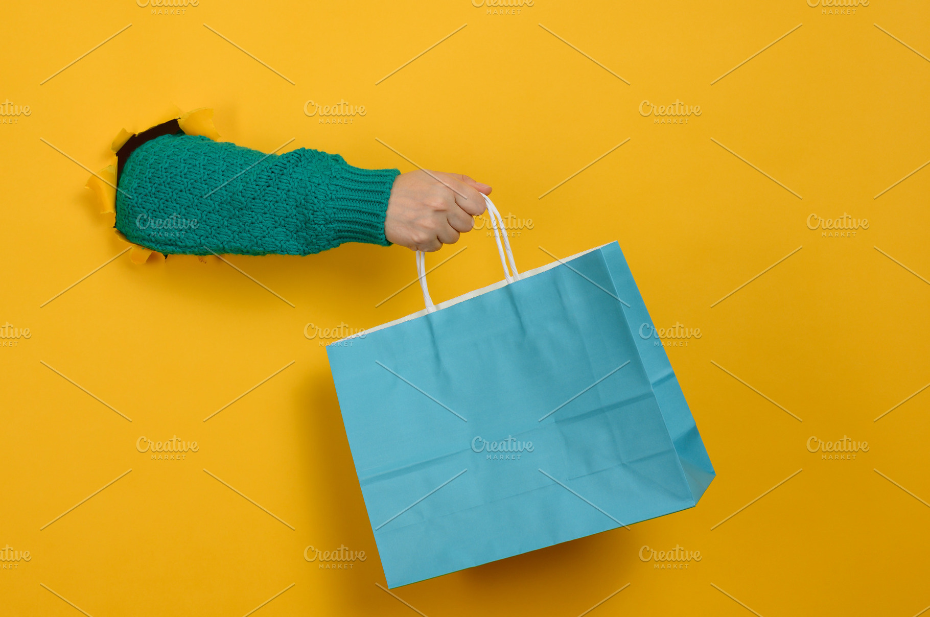 A woman's hand, clad in a green knitted sweater, holds a blue pa, a Person Photo by ndanko
