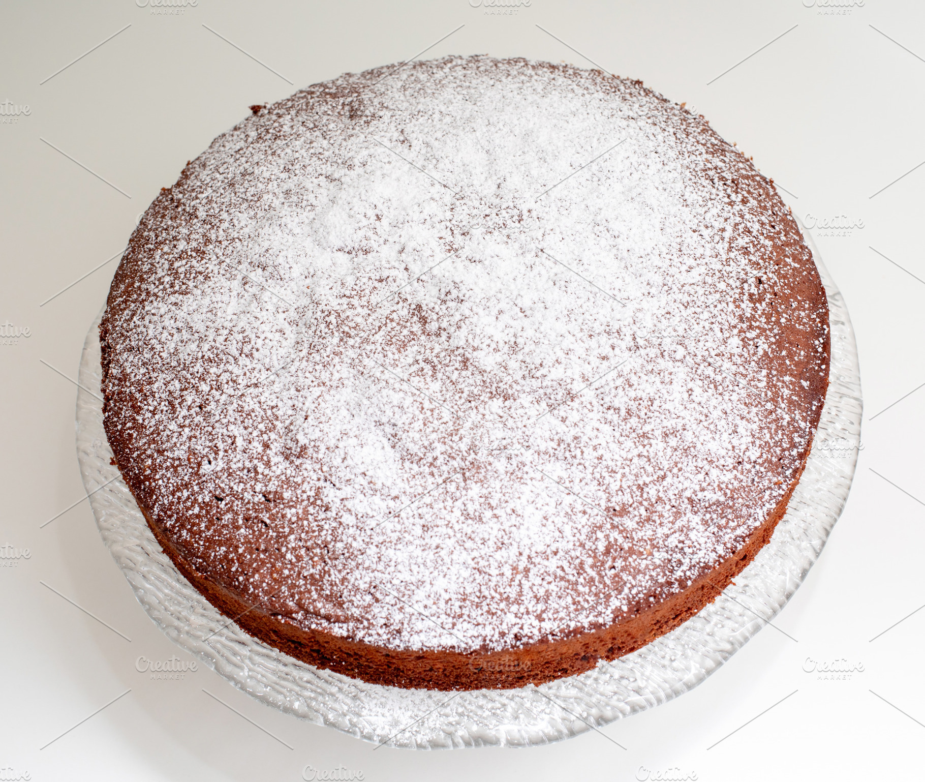 Delicious homemade caprese cake resting on a glass cake stand, sprinkled with p, a Food & Drink Photo by Antonio Gravante Market