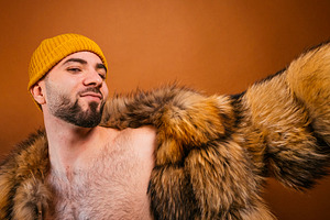 Assertive man posing with fur coat and beanie, a Photo by karrastock