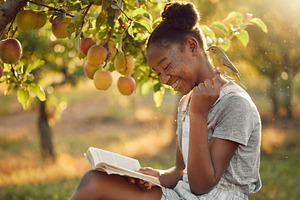 Young girl reading a book under an apple tree, a Person Photo by DanFLCreativo