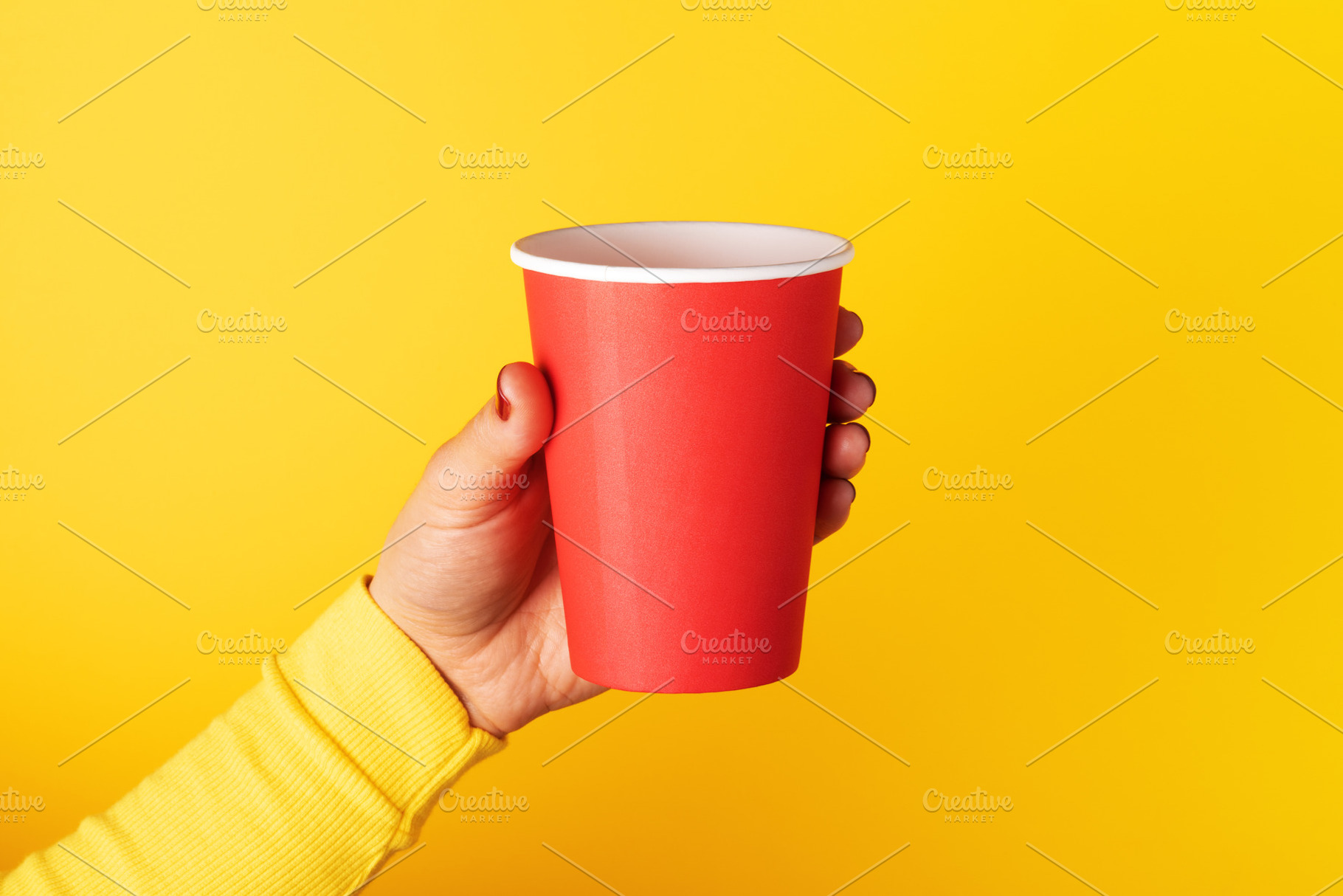 Hand holding a red paper cup against a vivid yellow background,, a Food & Drink Photo by Ales Munt