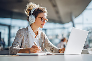 Woman working on laptop with headphones in office, a Person Photo by AlyaAnd