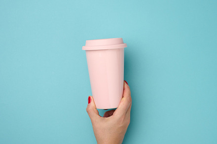 female hand holding a pink ceramic mug with a plastic lid on a b, a Food & Drink Photo by ndanko