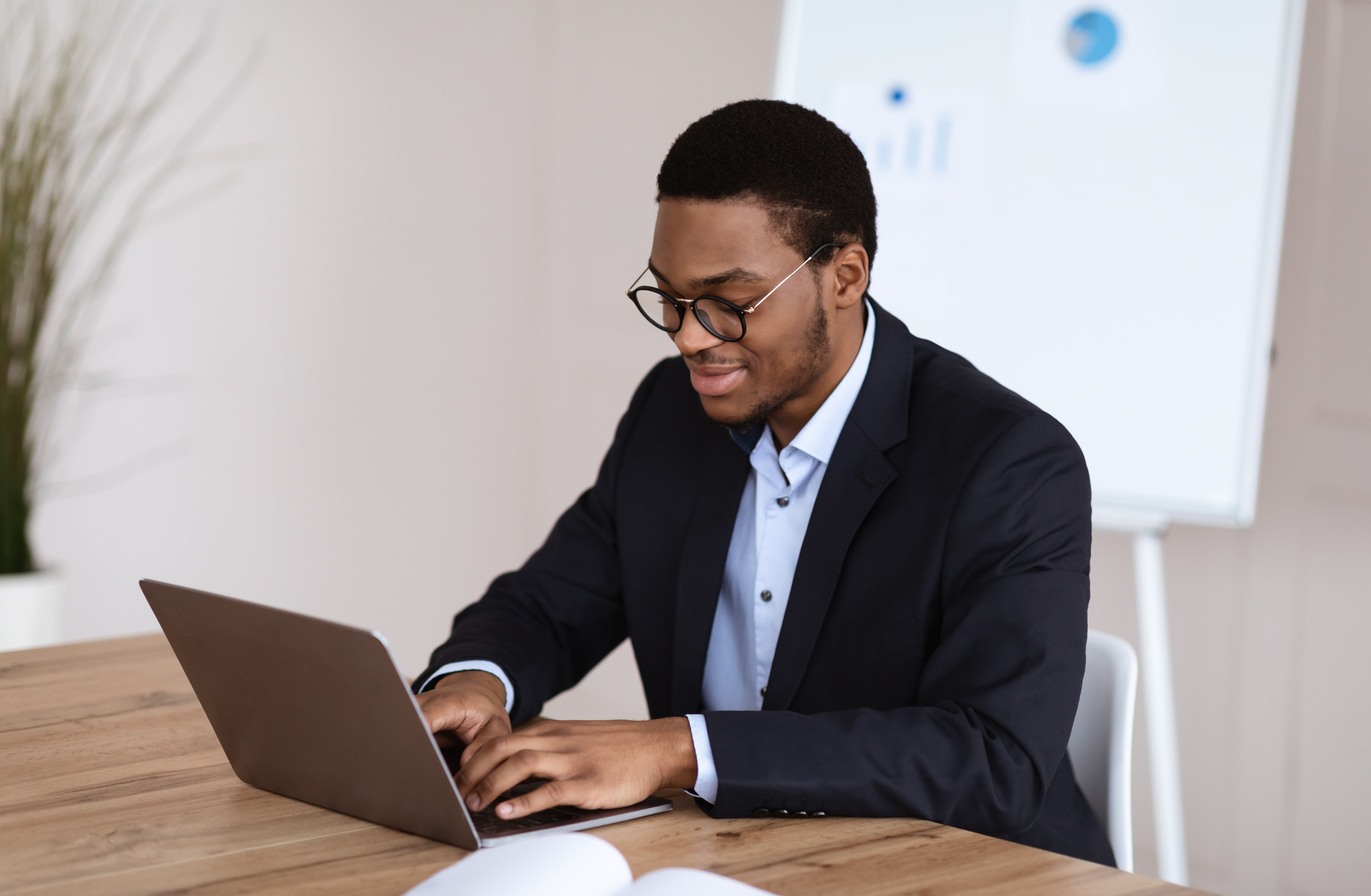 Young black manager smiling while working with laptop, office interior ...