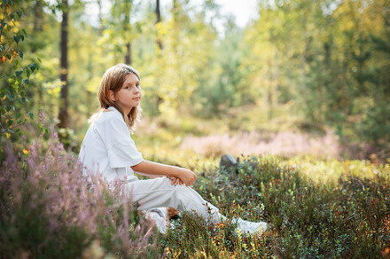 A young child sitting quietly in a serene forest, surrounded by, a Person Photo by Olena Rudo
