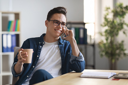Work Break. Millennial Guy Relaxing In Office With Cellphone And Coffee