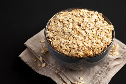 Wholegrain Oat Flakes in a Bowl on a black background, side view, a Food & Drink Photo by LiudmylaChuhunova