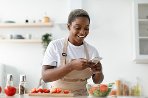 Smiling young pretty african american woman blogger in apron making photo of sa, a Person Photo by Prostock-Studio