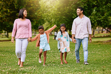 Two adorable little girls walking outside at park with parents. Sibling sisters out for a walk outdoors with their mother and father on a sunny summer day. Enjoying nature and family, a Photo by Peopleimages.com