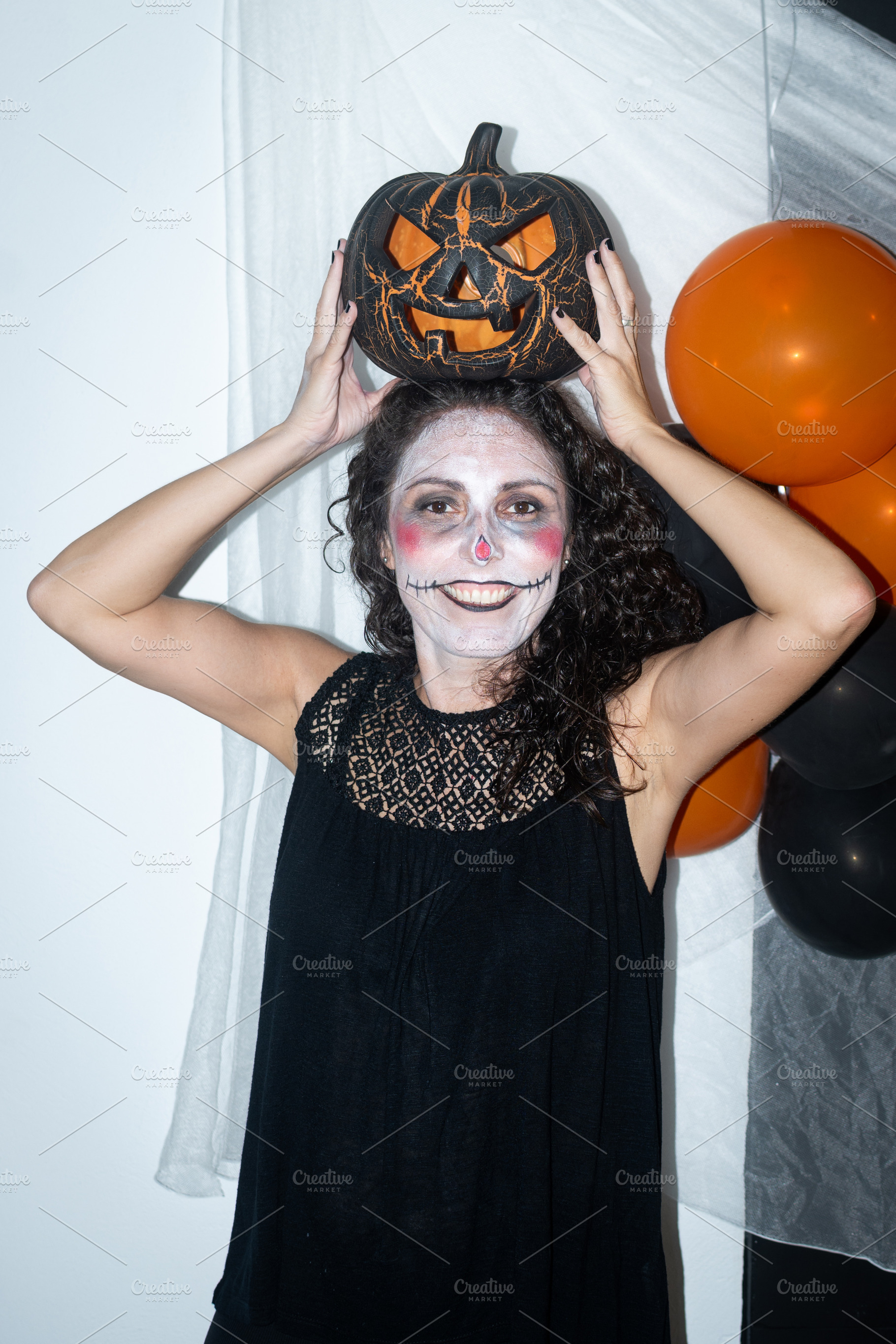 Woman with Halloween makeup holding pumpkin decoration on her head, a Person Photo by etorres69