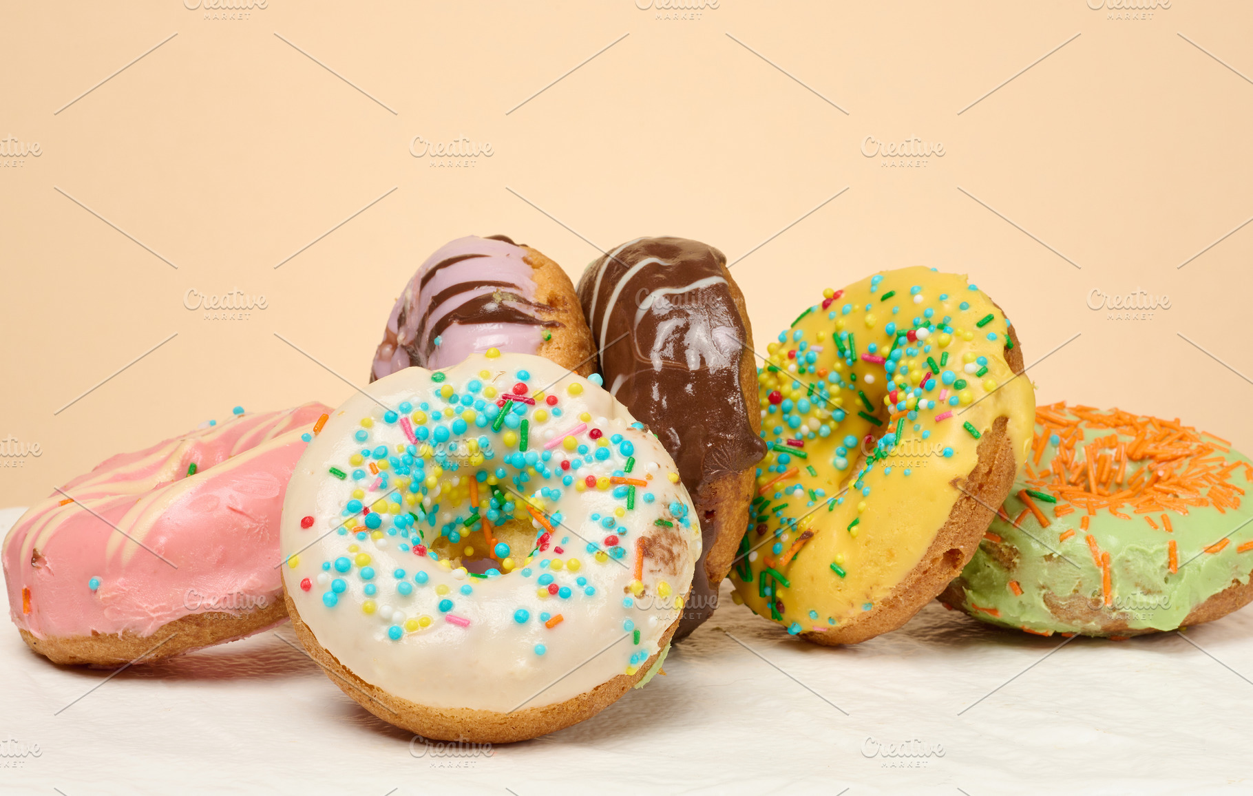 Stack of donuts with different toppings and glazes, beige backgr, a Food & Drink Photo by ndanko