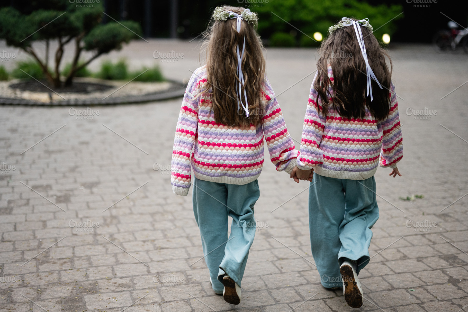 Two children holding hands dressed in colorful sweaters, walking outdoors toget, a Photo by AS photostudio