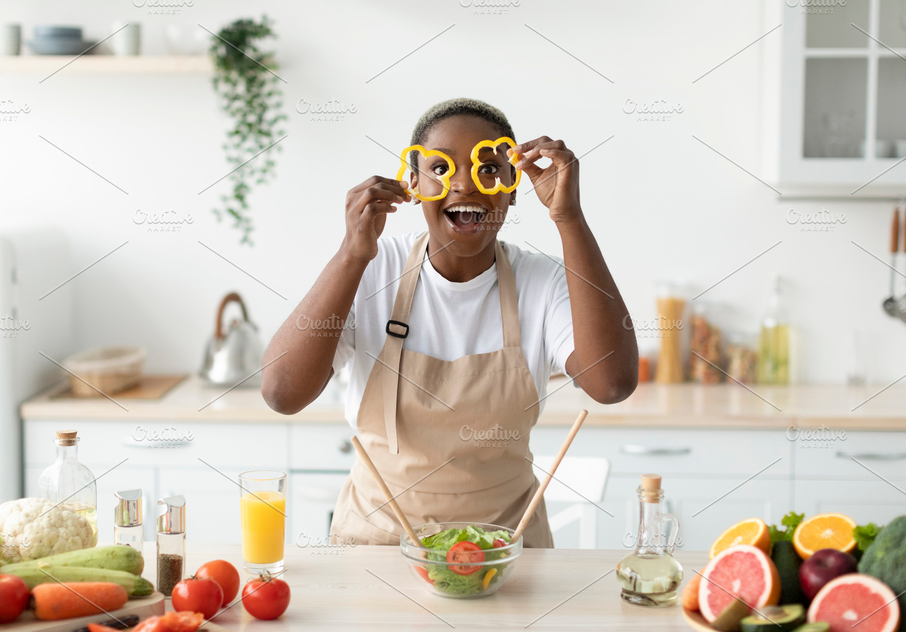 Glad young black female in apron have fun, make salad, puts pieces of paprika t, a Person Photo by Prostock-Studio