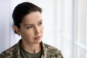 Thoughtful female soldier wearing camouflage uniform looking through window at, a Photo by Prostock-Studio