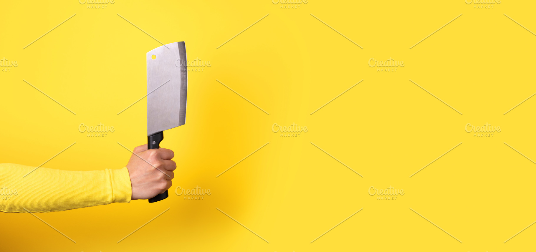 Close-up of a hand gripping a meat cleaver against a bright yell, a Food & Drink Photo by Ales Munt