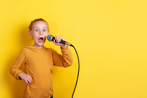 Excited red-haired girl in yellow sweater holding microphone, si, a Person Photo by Ales Munt