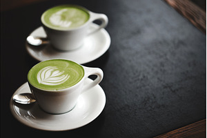 Two cups of matcha latte on black