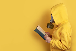 Side view of a person in yellow hoodie and gas mask reading a bo, a Person Photo by Ales Munt