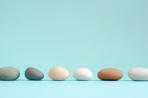 Assorted natural pebbles lined up on a light blue background, an Abstract Photo by Natalia Klenova's Shop