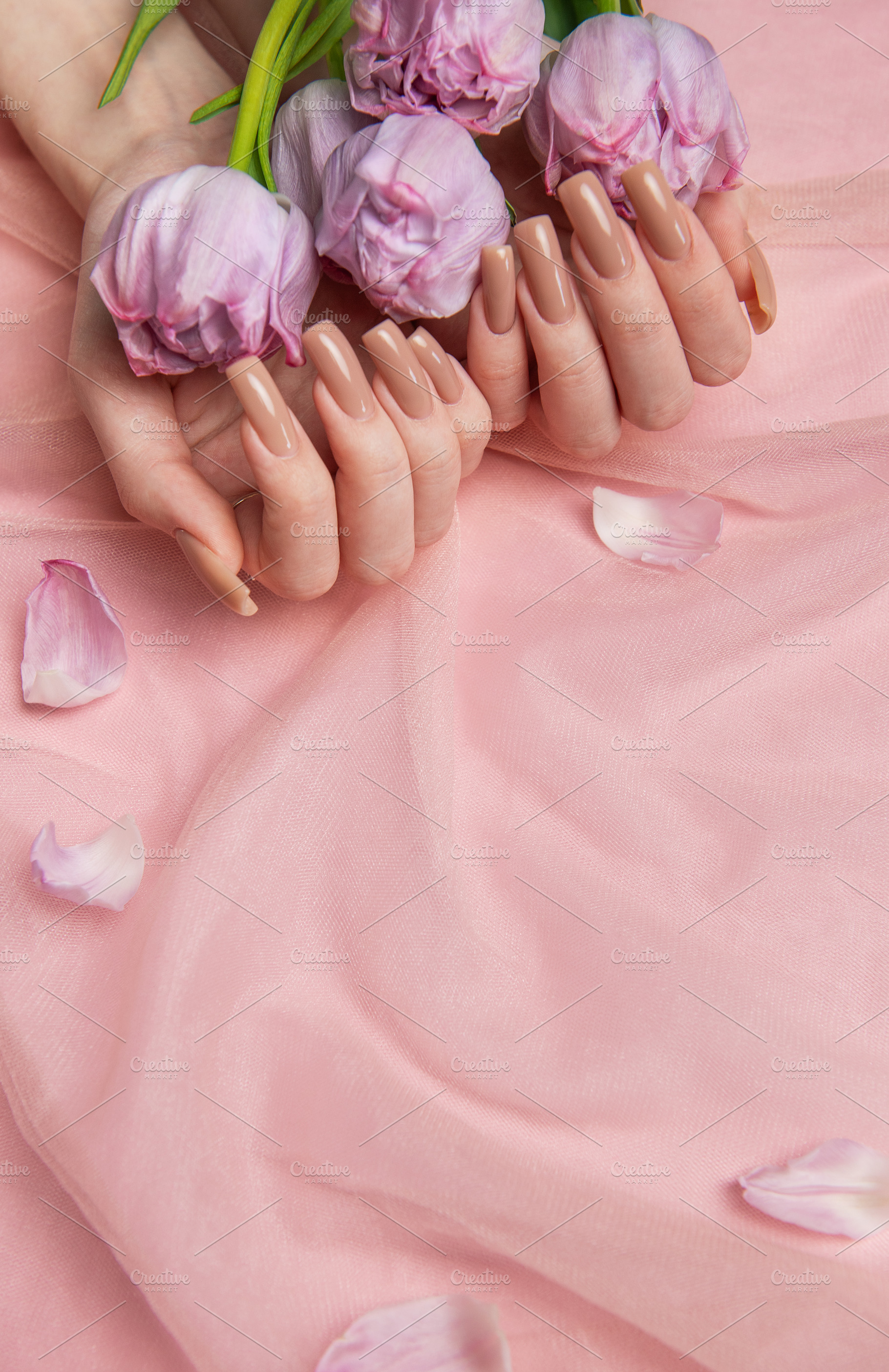 Woman hands holding pink tulips showing nude manicure on pink ba, a Beauty & Fashion Photo by Olena Rudo