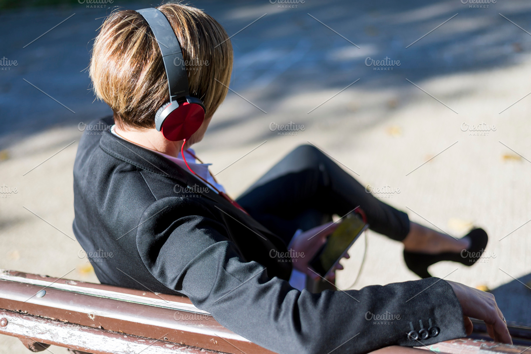Businesswoman listening to music on park bench, a Photo by RF Images