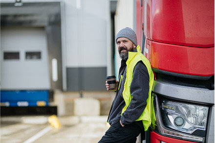 Truck driver leaning against red, a Transportation Photo by HalfPoint