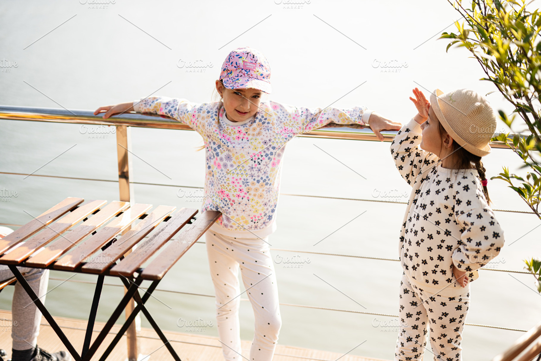 Two young girls enjoying an outdoor moment near a railing and table, a Person Photo by AS photostudio