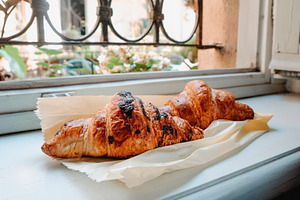 two croissants on parchment paper by a windowsill, a Photo by Nito