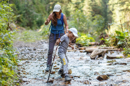 Young woman fording the stream with her son in mountains, a Sports & Recreation Photo by serkum