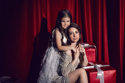 beautiful young woman in a shiny dress is sitting with a daughter child on red, a Person Photo by SaulichPhoto